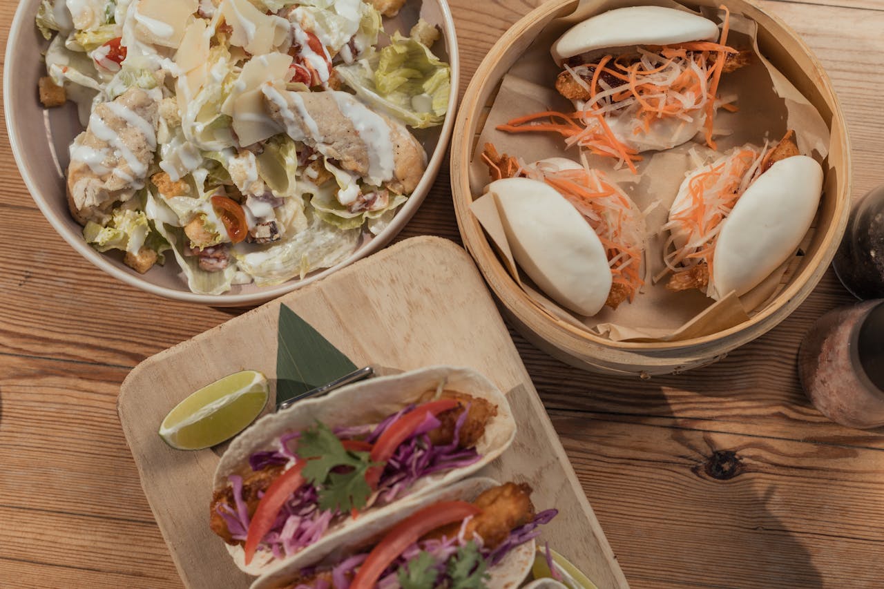 Delicious spread of tacos, bao buns, and salad presented on a wooden table, perfect for a casual dining theme.