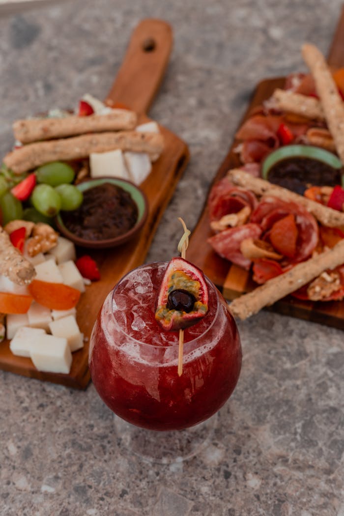 Iced cocktail with charcuterie boards featuring cheese, fruit, and meats on a rustic table.
